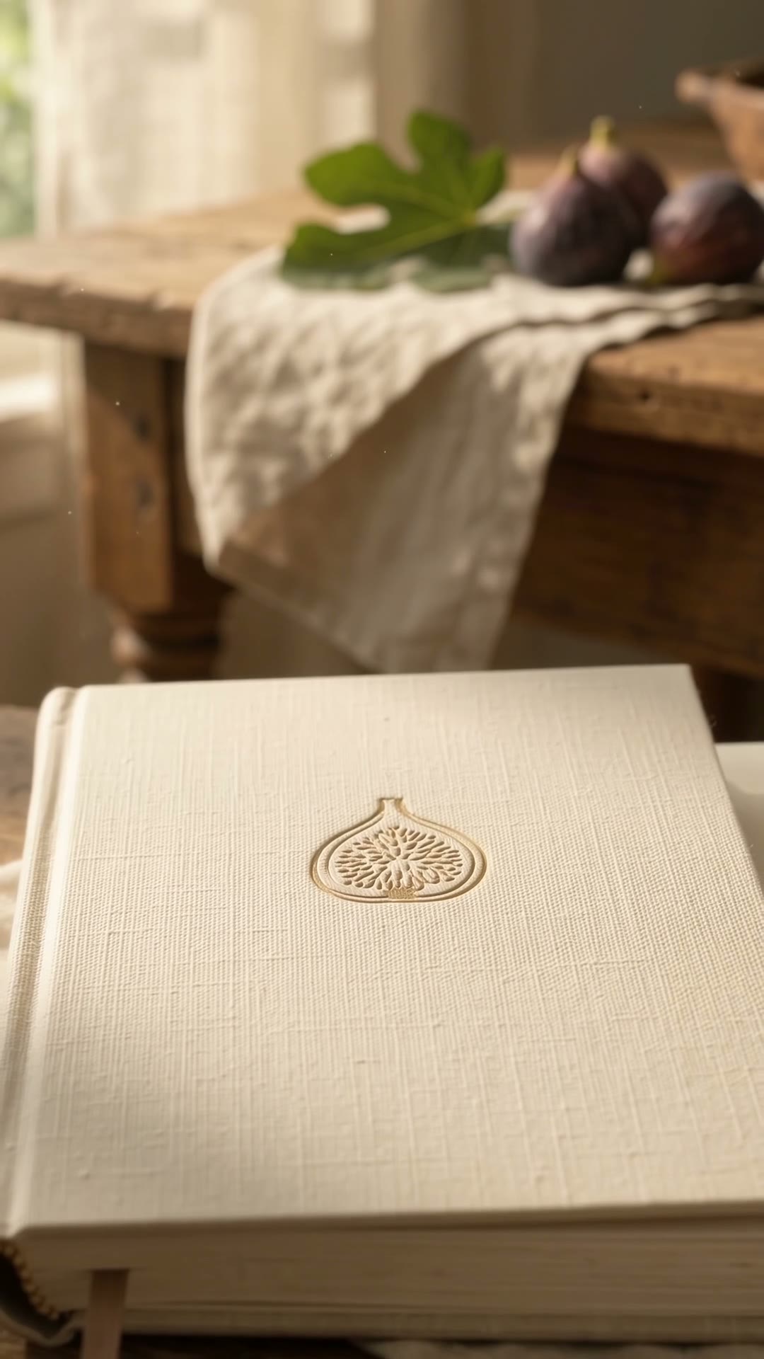 A recipe journal opens and a jar of dark fig jam rises above the page beside a cut fig